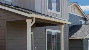 Beige gutter installed on a house with grey siding and vinyl windows.