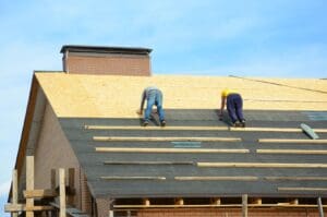 Asphalt roofing shingles. Building contractors laying bitumen waterproofing membrane berofe laying asphalt shingles roofing. Roofers Install, Repair Asphalt Shingles House Rooftop