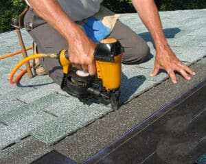Roofer uses nail gun to attach asphalt shingles to roof