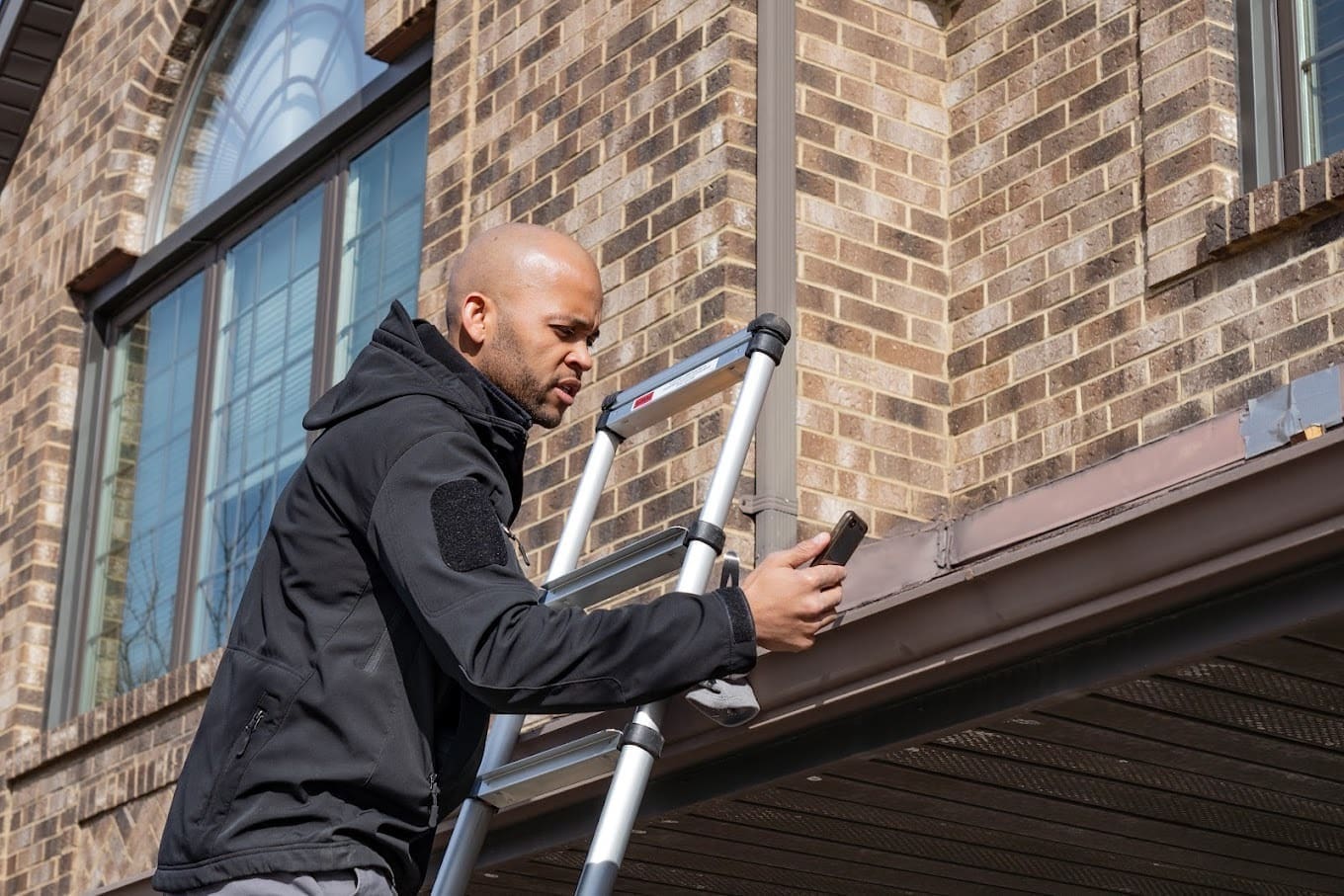 person on ladder inspecting gutters